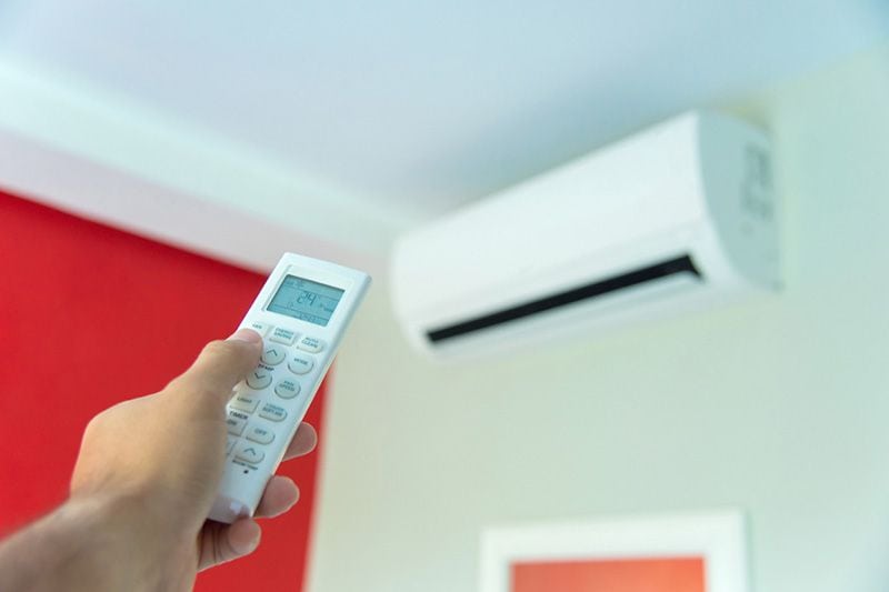Image of someone holding remote with a ductless system. Ductless ACs Improve Indoor Air Quality and Control Humidity.