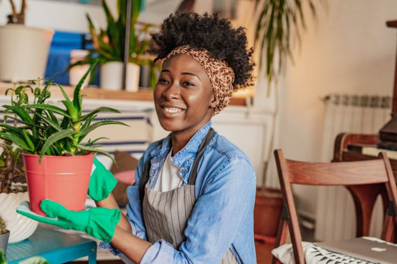 woman taking care of plants at her home, she is holding a plant and smiling.