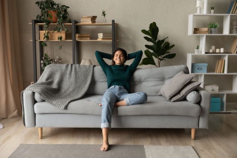 How a Whole-House Humidifier Keeps You Healthy. Image shows woman sitting and relaxing on couch.
