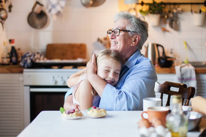 Happy grandmother is hugging granddaughter in cozy home kitchen.