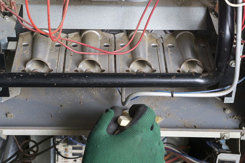 Image of someone working on a furnace with green gloves. 5 reasons to schedule a fall furnace clean and check.