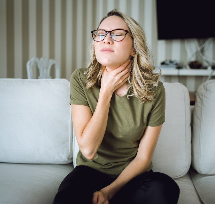 Young blonde woman with glasses grabbing her throat because it hurts from poor indoor air quality.